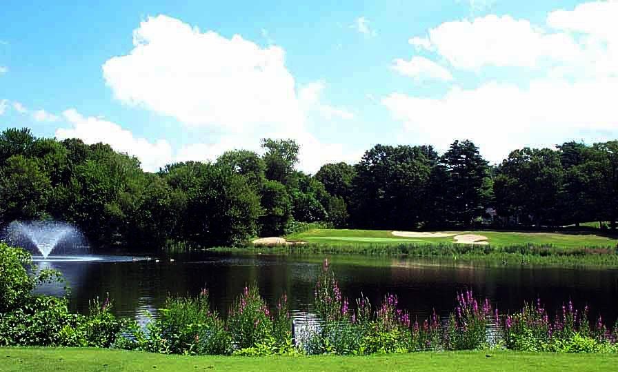 The ninth green seen across the pond, with a fountain and summer wildflowers